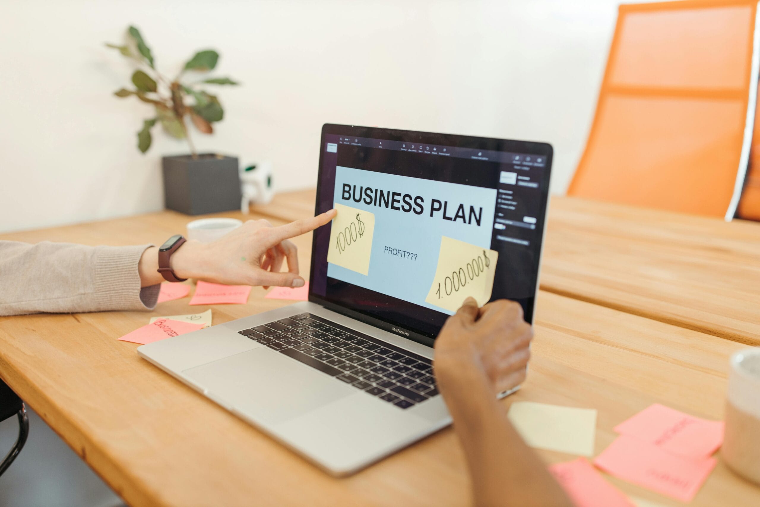 Dwie osoby pracujące przy laptopie, którego ekran wyświetla napis "BUSINESS PLAN". Na ekranie i biurku dookoła widoczne są karteczki samoprzylepne z notatkami i kwotami (np. 1000$ i 1.000.000$). Obraz symbolizuje budżetowanie, pakiety cenowe i planowanie finansowe współpracy z agencją content marketingu Contentologia.