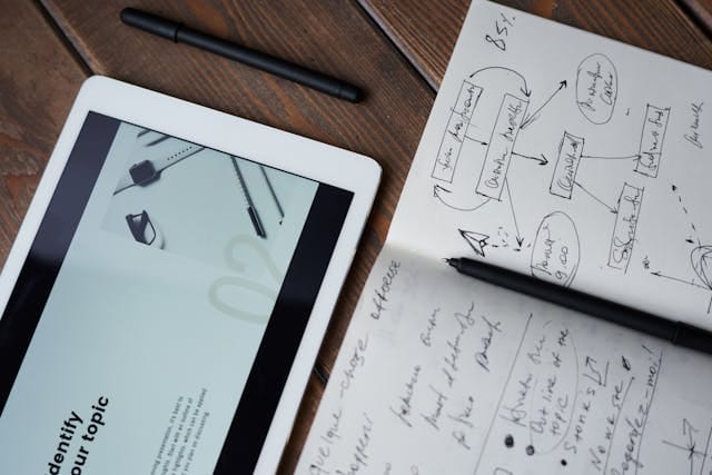  Zdjęcie przedstawia otwarty notatnik z odręcznymi schematami i notatkami, obok leży tablet z otwartą prezentacją. Ilustruje to etap burzy mózgów i planowania, ważny dla efektywnego Content marketing dla B2B w agencji interaktywnej Contentologia.