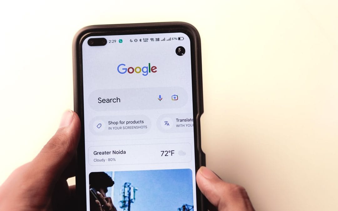 Zdjęcie wyróżniające do artykułu agencji Contentologia przedstawia pionowy kadr trzymanego w dłoniach smartfona, na którego ekranie widoczna jest aplikacja wyszukiwarki Google z logo, paskiem wyszukiwania oraz widżetem pogody i informacjami o lokalizacji, co idealnie nawiązuje do tematyki patentów Google, sygnałów behawioralnych i optymalizacji pod wyszukiwarki internetowe.
